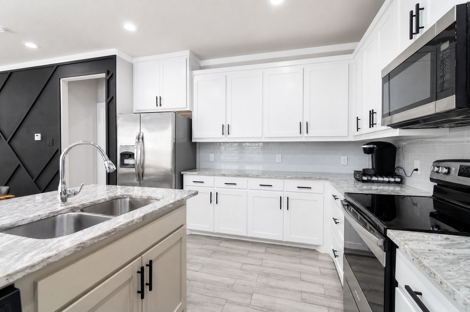 A modern kitchen with white cabinets, stainless steel appliances, and a marble countertop.