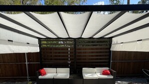 A patio area with a covered seating arrangement and a wooden fence in the background.