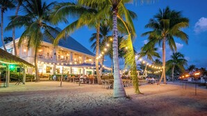 A beachfront hotel with outdoor seating and palm trees.