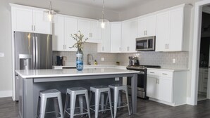 Een moderne keuken met witte kasten, roestvrijstalen apparatuur en een centraal eiland met barkrukken.