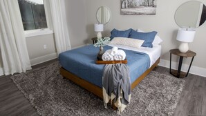 Een keurig opgemaakt slaapkamer met een bed, twee nachtkastjes, een raam met gordijnen, een spiegel aan de muur en een schilderij.