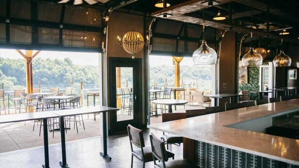 Een restaurant met terras, grote ramen en hangende lampen.