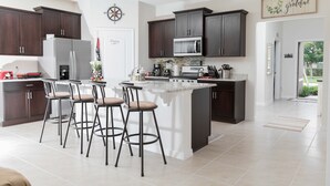 Una cocina moderna con armarios de madera oscura, una isla grande con taburetes de bar, un refrigerador y un microondas.