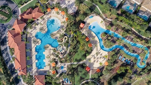 Vista aérea de un complejo turístico con varias piscinas, palmeras y un tobogán serpenteante.