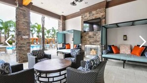 Un espacio lounge al aire libre con mobiliario de mimbre, una mesa redonda, una chimenea y un televisor montado en una pared de piedra.