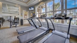 Un gimnasio con cintas de correr, máquinas de pesas y un televisor en la pared.