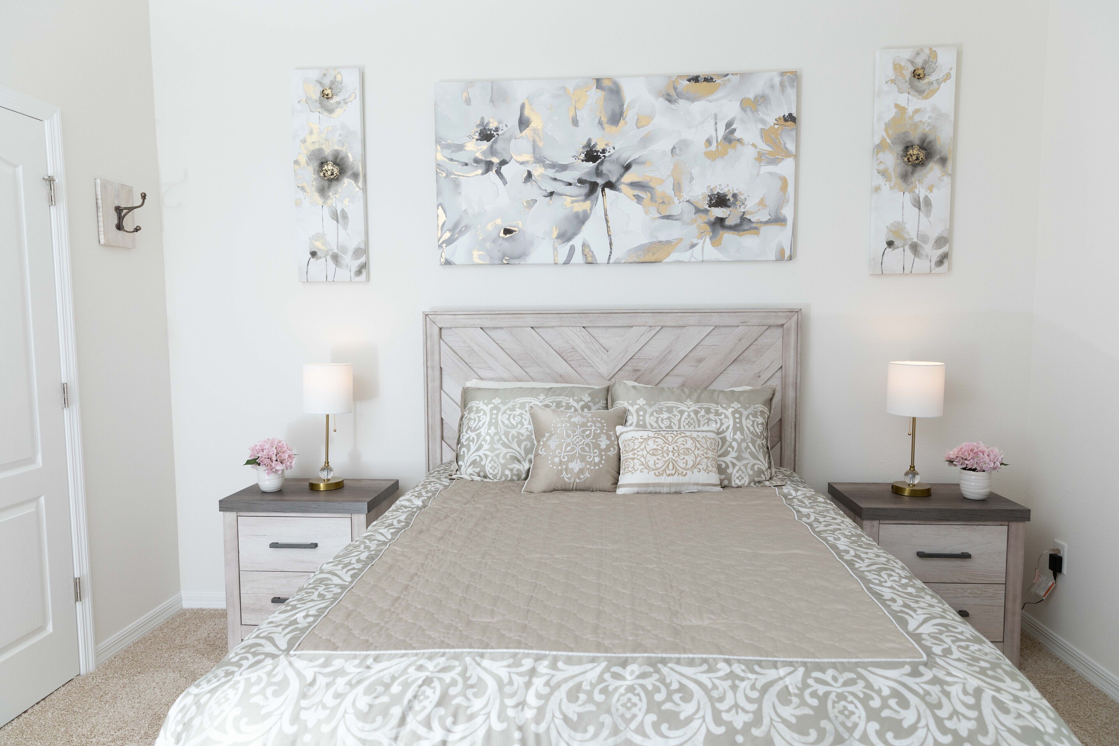 A bedroom with a large bed, two bedside tables, and three wall-mounted paintings.