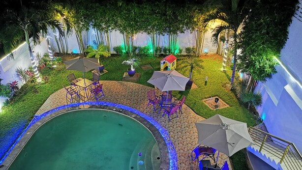Ein Pool mit gefliestem Deck und blauen LED-Leuchten. Liegestühle und Sonnenschirme stehen bereit, und es gibt eine kleine gebäudegleiche Struktur.