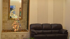 Ein Wohnzimmer mit einem braunen Ledersofa, einem Tisch mit einer Pflanze, einer Kristallleuchtreiter und einem wandmontierten Spiegel.