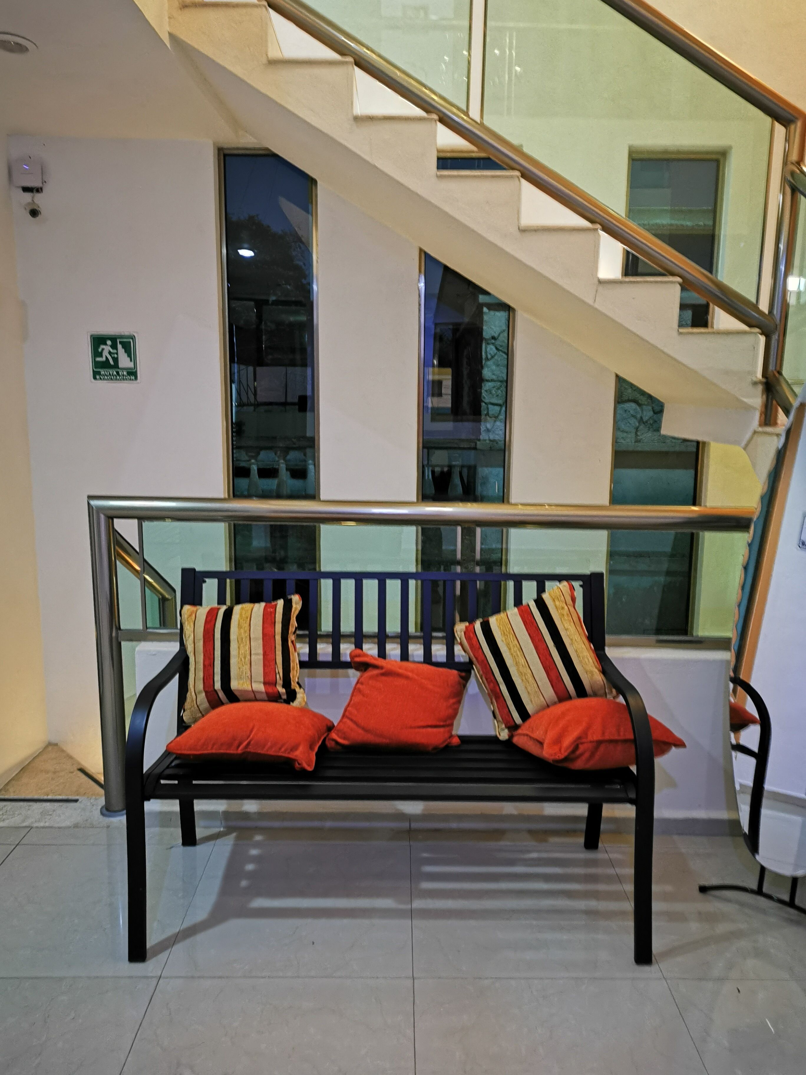 A bench with striped cushions in a modern building with a glass railing and a staircase.