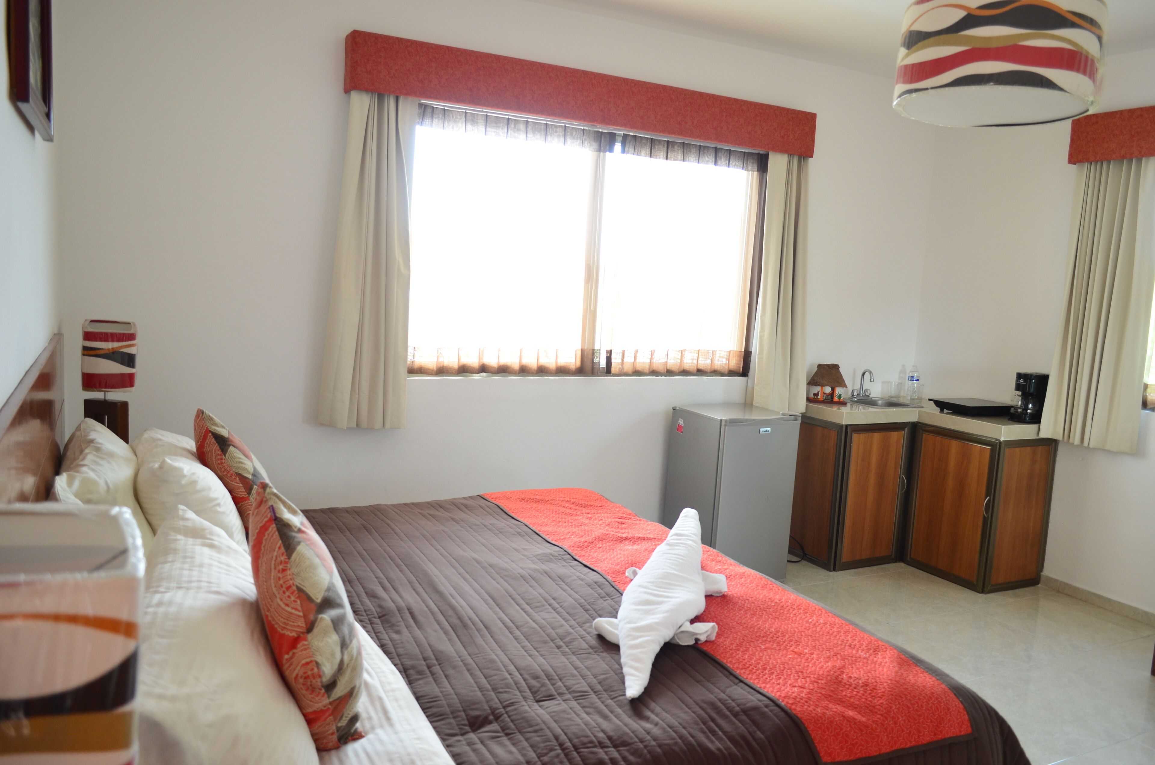A hotel room with a bed, a desk, a refrigerator, and a window with curtains.