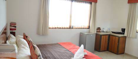 A hotel room with a bed, a desk, a refrigerator, and a window with curtains.