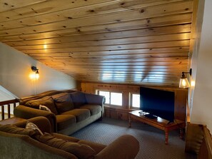 Un salon chaleureux avec un plafond en bois, un canapé, un téléviseur et une lampe.