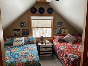 Cozy attic bedroom with two single beds, a dresser, and vinyl records on display.