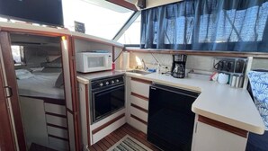 Una kitchenette compacta equipada con microondas, estufa y lavavajillas, un lavamanos pequeño y un ventanal con cortinas.