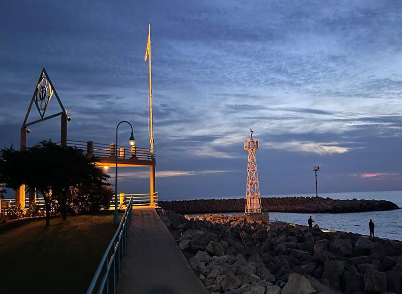 A coastal walkway with a metal fence, a tall light pole, and a rocky shoreline.