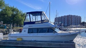 Un barco blanco amarrado en un puerto deportivo, con cielo despejado y edificios al fondo.