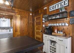 Une pièce chaleureuse aux murs en bois, avec un lit, un coin café équipé de tasses et d’une machine à café, et un panneau indiquant « CAFÉ ».