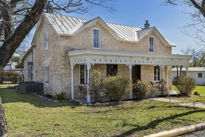 Une maison en pierre dotée d’un porche couvert, portant le numéro 420, entourée d’une cour verdoyante et d’arbres.