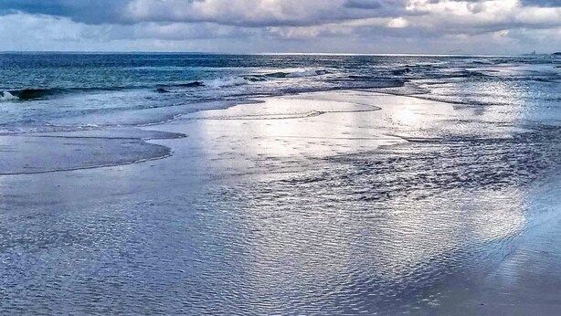 En strand med våd sand og en overskyet himmel.