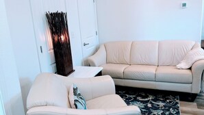 En stue med en beige sofa, en hvid lænestol, en dekorativ sort søjle og et tæppe med mønster.
