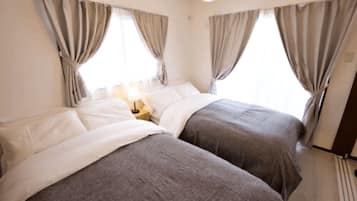 A hotel room with two beds, a nightstand, and curtains.