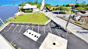 A parking lot with solar panels, a grassy area, and a view of the sea. - Ocean Terrace Sesoko 101 - Vacation Stay 28609V (Motobu)