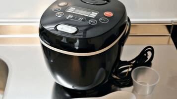 Una tetera eléctrica negra con pantalla digital, un cable de alimentación y una cuchara de silicona blanca sobre una encimera de cocina.
