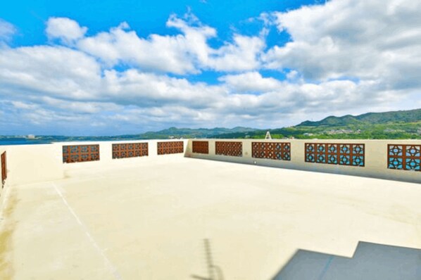 A rooftop terrace with a clear view of the surrounding landscape, including distant hills and a partly cloudy sky. - Ocean Terrace Sesoko 101 - Vacation Stay 28609V (Motobu)