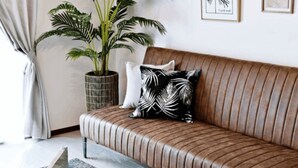 A brown leather sofa with a black and white patterned pillow, a glass coffee table, and a potted plant. - Ocean Terrace Sesoko 101 - Vacation Stay 28609V (Motobu)