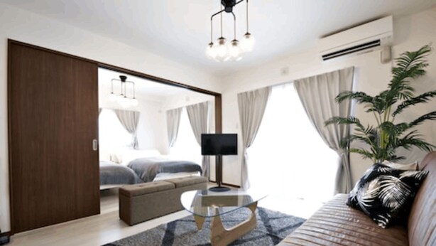 A modern hotel room with a sofa, a glass coffee table, a TV, and a large window with curtains. - Ocean Terrace Sesoko 101 - Vacation Stay 28609V (Motobu)