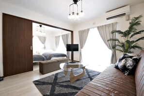A modern hotel room with a sofa, a glass coffee table, a TV, and a large window with curtains. - Ocean Terrace Sesoko 101 - Vacation Stay 28609V (Motobu)
