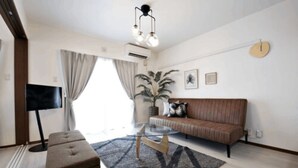 A modern living room with a sofa, a glass coffee table, a TV, and a large window with curtains. - Ocean Terrace Sesoko 101 - Vacation Stay 28609V (Motobu)
