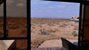 Une pièce dotée d’une grande fenêtre donnant sur un paysage aride et dégagé, avec une végétation clairsemée et un bâtiment situé au loin.