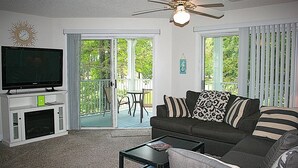 Un salon comprenant un téléviseur, un canapé, une table basse et un balcon avec une table et des chaises.