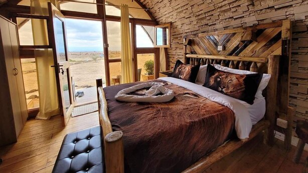 Ein Schlafzimmer mit einem großen Bett, einem Holzkopfende und Blick auf die Wüste durch große Fenster.