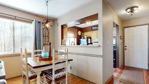 A dining area with a wooden table and chairs, a hanging light fixture, and a view into a kitchen area with cabinets and a refrigerator. - Warm & Inviting Ski Getaway w/ a Full Kitchen, Fireplace, & Furnished Deck (Sugar Mountain)