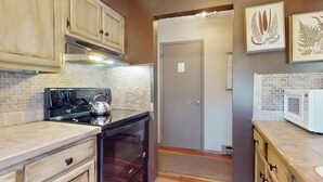 A kitchen with a stove, oven, and microwave. There are wooden cabinets and a door with a sign. - Warm & Inviting Ski Getaway w/ a Full Kitchen, Fireplace, & Furnished Deck (Sugar Mountain)