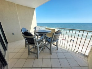 A balcony with a table and chairs, overlooking a beach.
