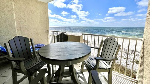 A round table with four chairs on a balcony overlooking a beach. - Tropical Winds 303 2 Bedroom Condo by RedAwning (Gulf Shores)