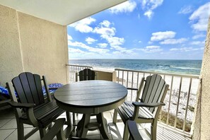 A round table with four chairs on a balcony overlooking a beach.