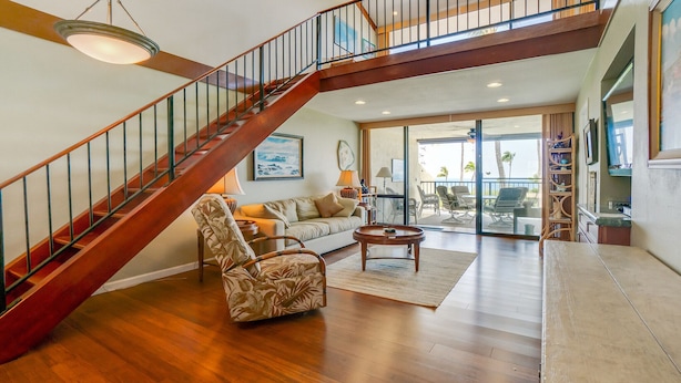 A spacious living room with a wooden staircase, a sofa, a patterned armchair, and a coffee table. - 2 Story top level AC unit 2 bdrms w/Large Loft with 2 twin beds & bathrm SUNSETS (Kailua-Kona)