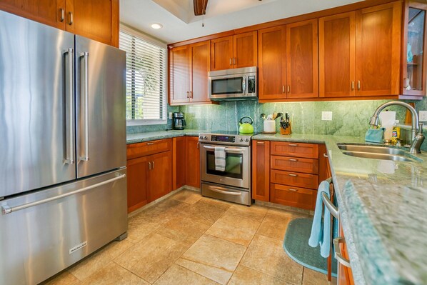 A kitchen with stainless steel appliances, wooden cabinets, a microwave, and a sink.