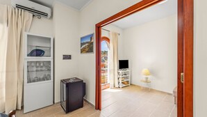 Een kamer met een televisie, een klein kastje, een plank met glazen, een deur naar een andere kamer en een raam met uitzicht.