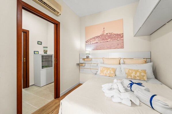 Habitación de hotel con cama, mesita de noche, lámpara de pared, cuadro enmarcado y puerta que da a un baño.