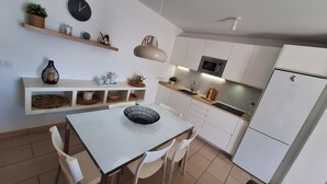A modern kitchen with white cabinetry, a dining table with chairs, a hanging light fixture, and a clock on the wall. - Vacation Apartment Arenas del Porís with Sea View and Shared Pool (Arico)