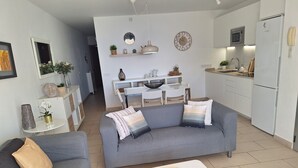 A modern living room with a grey sofa, a white coffee table, and a kitchen area with white cabinets and appliances. - Vacation Apartment Arenas del Porís with Sea View and Shared Pool (Arico)