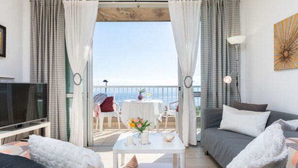 A modern living room with a television, sofa, coffee table, and a balcony with a view. - Vacation Apartment Arenas del Porís with Sea View and Shared Pool (Arico)