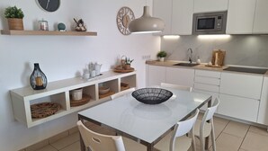 A modern kitchen with white cabinetry, a dining table with chairs, a hanging light fixture, and a clock on the wall. - Vacation Apartment Arenas del Porís with Sea View and Shared Pool (Arico)