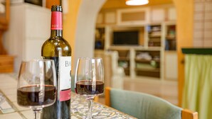 Une bouteille de vin et deux verres sur une table, dans une pièce dont le sol est recouvert de carreaux et où se trouve une chaise verte.